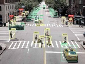 Street scene annotated with bounding boxes identifying people, vehicles, bicycles, and traffic lights for computer vision training