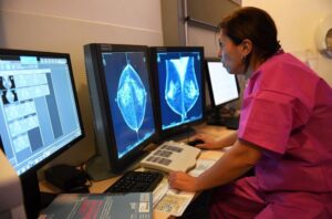 Healthcare professional in pink scrubs analyzes mammography scans on multiple monitors.