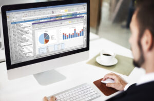 Man analyzing charts and spreadsheets on a computer with graphs and a pie chart.